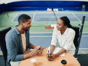 How Athletic Directors Can Conduct Effective Evaluations, Part 1: Coach Evaluations An athletic director and a coach sit across from each other at a table during a meeting, reviewing notes and discussing evaluation goals in a professional setting.