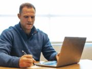 How Athletic Directors Can Conduct Effective Evaluations, Part 3: Athletic Director Evaluations Athletic director seated at a desk, focused on a laptop, reviewing documents — representing the behind-the-scenes administrative work and evaluations central to leading athletic programs.