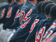 Integrating Sports Psychology into Athletic Programs A group of baseball players sit closely together on the dugout bench, wearing uniforms and caps, watching the game with focus and camaraderie. The image conveys teamwork, concentration, and the shared experience of athletes supporting one another — reflecting the article’s theme of integrating sports psychology into athletic programs to strengthen both mental and physical performance.