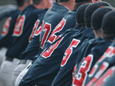 Integrating Sports Psychology into Athletic Programs A group of baseball players sit closely together on the dugout bench, wearing uniforms and caps, watching the game with focus and camaraderie. The image conveys teamwork, concentration, and the shared experience of athletes supporting one another — reflecting the article’s theme of integrating sports psychology into athletic programs to strengthen both mental and physical performance.