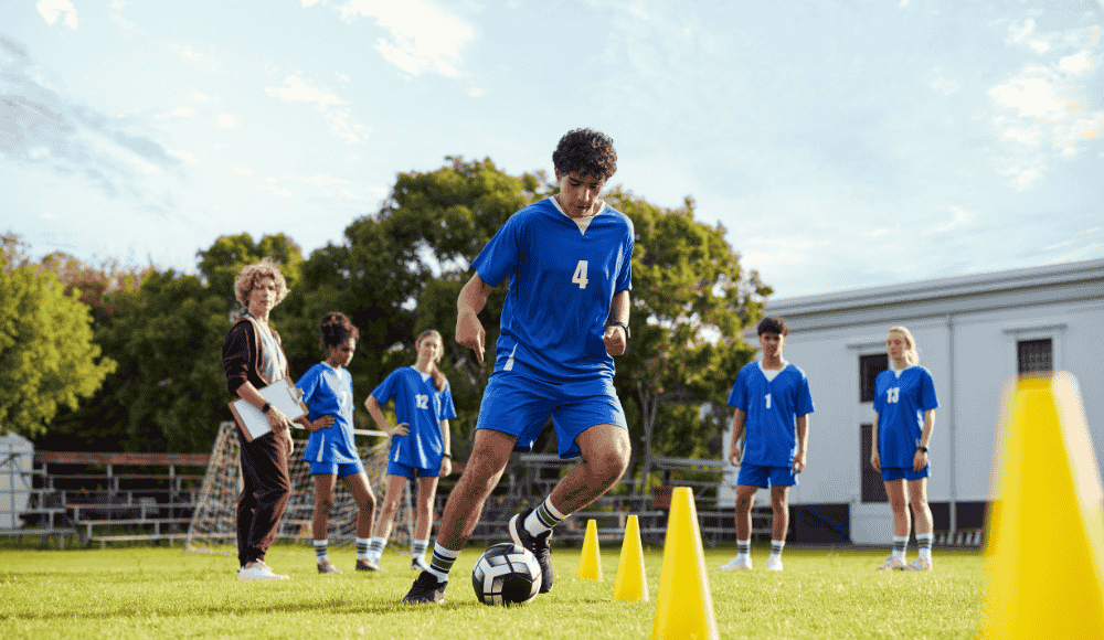 Can High School Sports Win Back the Spotlight? High school soccer players practice on a grassy field at sunset, wearing school uniforms and running drills. The image highlights the spirit of teamwork and school pride amid growing competition from private club sports programs.