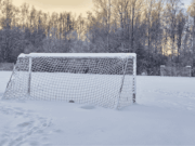 A Practical Guide to Winter Athletic Facility Maintenance A snow-covered soccer field with a goal partially buried in snow, showing an empty, wintery athletic facility with no players or activity.