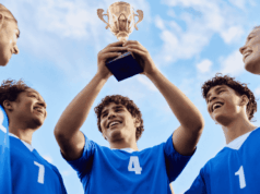 5 Scholastic Sports Trends Shaping 2026 High school athletes in blue jerseys celebrate a championship win by raising a trophy together, representing scholastic sports trends, student-athlete success, and the future of athletic programs heading into 2026.