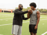 Why Athletic Trainers Are Leaving and What Athletic Directors Can Do About It Athletic trainer evaluating a student-athlete’s shoulder during football practice, illustrating athletic trainer responsibilities, sports injury care, and the importance of retention in school athletic programs