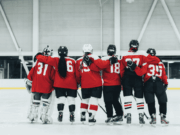 The US Men’s Hockey Controversy Proves There’s Still Work To Be Done Women’s hockey players in red jerseys stand arm in arm on the ice after a championship game, symbolizing unity, equality, and respect in women’s sports amid ongoing gender equity discussions.